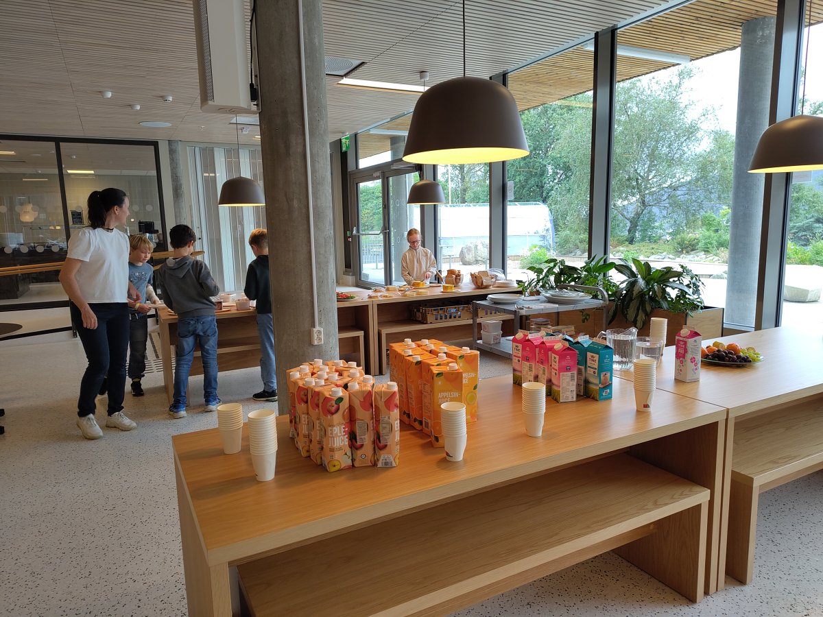 Lunsjmat: Jus og mjølk i forgrunnen, nokre juniormusikantar som smører seg lunsj i bakgrunnen.